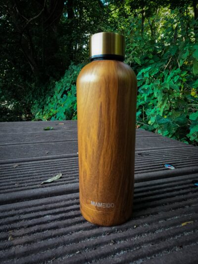 Eine holzfarbene MAMEIDO Edelstahl Thermosflasche auf einem Steg